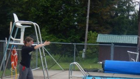 Campers on the side of the swimming pool watching the instructor teach a lesson. 