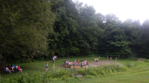 distance shot showing youth at picnic table on left, playing gaga in center, and playing volleyball on right during free time.