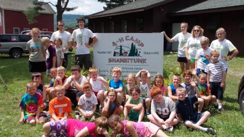 campers sitting in front of Camp Shankitunk sign with counselors standing in back 
