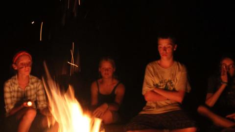 campers sit outside around a camp fire at night 