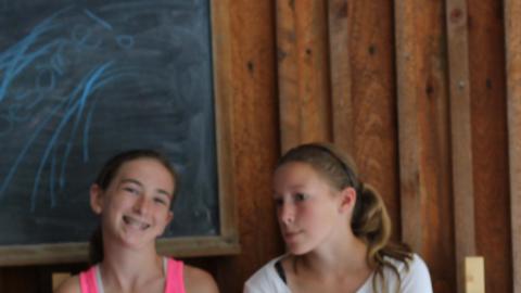 two campers sit on bench outside of camp building