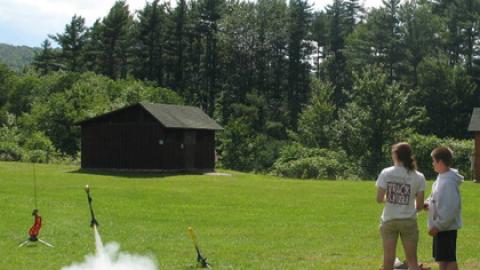 Camper stands with counselor and pushes the button to fire his rocket up into the air.