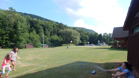 counselor sitting with hose and holding the end to spray two campers running toward them.