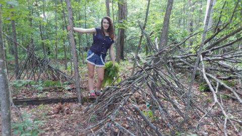Youth stands on the start of a shelter in the woods. 