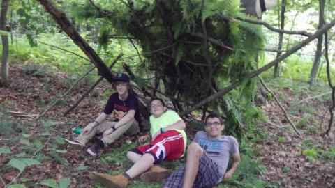 Campers sitting under a shelter made out of foliage. 
