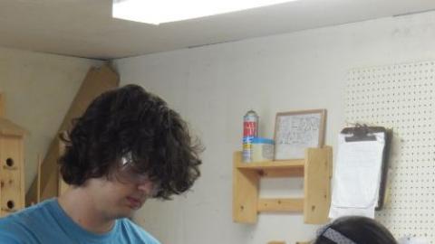 Camper working on a wood project with the help of an older youth. 